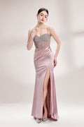 A woman stands against a light background, wearing a pink satin gown with a beaded, sheer bodice. It has thin straps, a ruched skirt, and a high side slit. The contrast of the sparkling beads and smooth satin fabric exudes elegance, perfect for formal galas or evening events, radiating charm.1