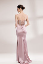 A woman stands against a light background, wearing a pink satin gown with a beaded, sheer bodice. It has thin straps, a ruched skirt, and a high side slit. The contrast of the sparkling beads and smooth satin fabric exudes elegance, perfect for formal galas or evening events, radiating charm.2