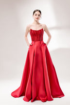 Against a light - hued background, a woman wears a red satin gown with a strapless, lace - detailed bodice and pockets. It has a voluminous skirt, combining romance and functionality. The vibrant red color and elegant design radiate confidence, perfect for formal events like weddings or award ceremonies.1