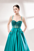 A woman stands against a light background, wearing a teal satin gown. It has thin straps, a sweetheart neckline, and a voluminous skirt. The bodice features sheer fabric with bead embellishments, combining elegance and romance. Perfect for formal events like weddings, it exudes charm.4