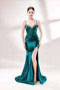 Set against a light background, a woman wears a teal satin gown with a bejeweled, sheer bodice. It has thin straps, a sweetheart neckline, and a mermaid - shaped skirt with a high side slit. The sparkling embellishments and smooth satin fabric exude elegance, ideal for galas or formal dinners.1