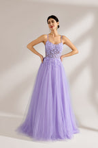 Set against a light backdrop, a woman wears a lavender tulle gown. It has thin straps, a sweetheart neckline with intricate lace embroidery on the bodice, and a flowing tulle skirt. The graceful design gives off a romantic and ethereal vibe, ideal for formal occasions such as proms or weddings.1