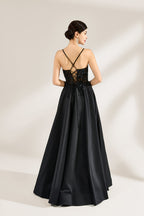 A woman stands against a light background, wearing a black satin gown. The bodice features thin straps, a draped neckline, and beaded embroidery. A high side slit adds allure, combining elegance and sexiness. Perfect for formal events like galas or evening parties, exuding sophistication.2