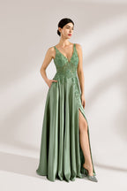 A woman with an elegant updo and a poised stance wears a sage - green satin gown. It has thin straps, a lace - detailed, V - neck bodice, and a high side slit. Paired with silver - tone heels, the outfit radiates grace, perfect for formal events like galas or weddings.2
