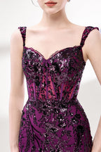 Set against a light background, a woman wears a purple tulle gown embellished with sequin embroidery. It has thin straps, a sweetheart neckline, a sheer bodice patterned with florals, and a mermaid skirt with a high side slit. Silver heels complete the look, with the sparkling sequins and refined silhouette ideal for proms or formal dinners.3