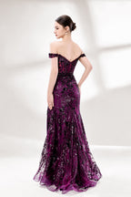 Set against a light background, a woman wears a purple tulle gown embellished with sequin embroidery. It has thin straps, a sweetheart neckline, a sheer bodice patterned with florals, and a mermaid skirt with a high side slit. Silver heels complete the look, with the sparkling sequins and refined silhouette ideal for proms or formal dinners.2