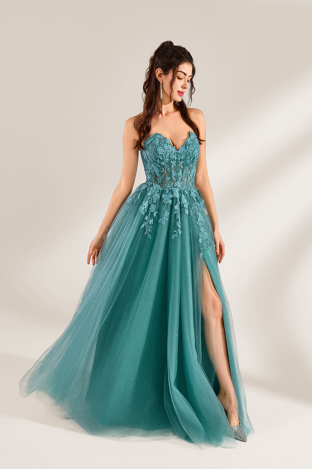 In front of a light - colored background, a woman is dressed in a teal tulle strapless gown. It has a sweetheart neckline, with the bodice adorned with delicate lace embroidery, and a high side slit. The voluminous tulle skirt, which has a slight shimmer, gives an elegant and romantic appearance, ideal for formal events such as proms or weddings.6