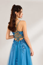 A woman stands against a light background, wearing a blue tulle gown. It features thin straps, a deep V - neckline, intricate floral appliqués with sequins on the bodice, and a high side slit. The voluminous tulle skirt creates a romantic and glamorous look, perfect for formal events like proms or weddings.6