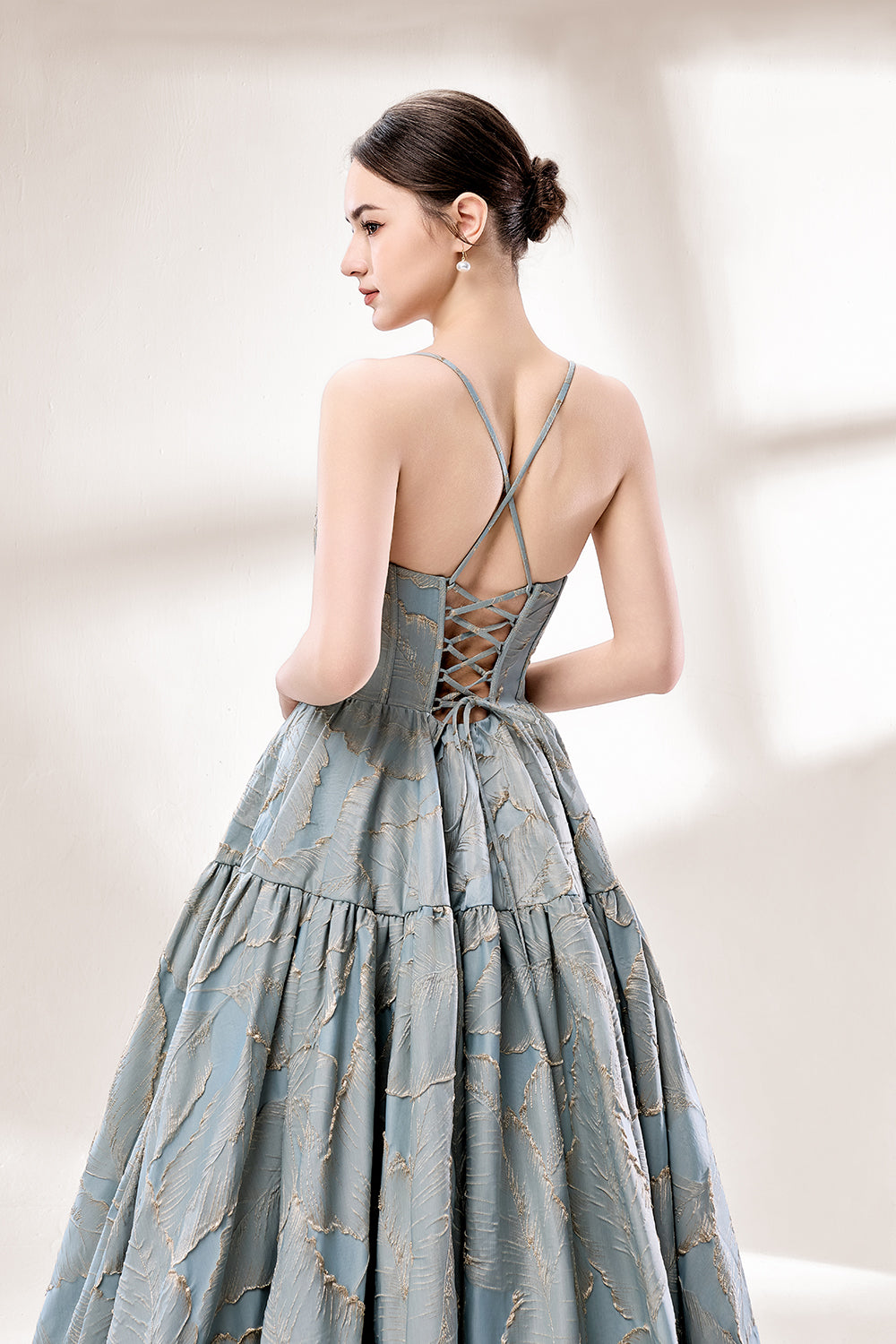 A woman stands against a light background, wearing a light - blue, tiered gown with gold - toned feather patterns. It has thin straps, a deep V - neckline, and a voluminous skirt. The unique jacquard design and elegant silhouette exude romance, perfect for formal events like garden parties or daytime weddings.7