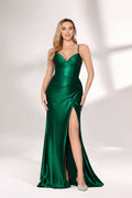 A woman with long, wavy blonde hair and soft natural makeup wears a striking emerald-green evening gown. It has delicate spaghetti straps, a deep V-neck, and a form-fitting bodice that flows into a floor-length skirt with a dramatic high side slit. The satin-like fabric shimmers, boosting its elegance. She pairs it with sleek light-colored heels, standing against a bright, minimalist backdrop that makes the vibrant green and sophisticated design stand out—ideal for formal events like galas or weddings.01
