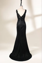 A photograph of a black, floor-length evening gown with a deep V-neck and lace detailing, featuring a thigh-high slit on the left side. The dress is displayed on a white mannequin with a black stand against a soft, beige background with diffused lighting creating gentle shadows. The gown exudes elegance and sophistication.32645.2