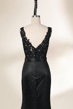 A photograph of a black, floor-length evening gown with a deep V-neck and lace detailing, featuring a thigh-high slit on the left side. The dress is displayed on a white mannequin with a black stand against a soft, beige background with diffused lighting creating gentle shadows. The gown exudes elegance and sophistication.32645.6