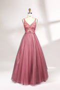 Photograph of a mannequin showcasing a floor-length, sleeveless, pink tulle gown with intricate lace detailing on the bodice and neckline. The gown features a fitted waist and flares out into a voluminous skirt, creating a ballerina-style silhouette. The mannequin stands against a plain white background with soft, diffused lighting casting subtle shadows.01