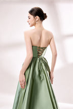 photograph of a woman in a backless, strapless, emerald green satin gown, standing against a white studio background, soft shadows, elegant, classic style, smooth fabric texture, hair in an elegant updo, long flowing gown, no visible accessories, minimalistic setting, studio lighting, elegant and sophisticated, full-length dress, high slit, backless design, full body shot, serene and graceful atmosphere.33110B-05
