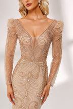 A woman stands against a light background, wearing a champagne - colored mermaid - style gown. It features a deep V - neckline, intricate beadwork throughout, and long sheer sleeves. The elegant design creates a glamorous and sophisticated look, perfect for formal events like galas or weddings.4