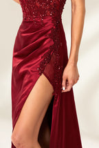 Photograph of a slender, attractive blonde woman with wavy hair. She wears a floor-length, off-shoulder, burgundy satin gown with a high slit and intricate beaded bodice. Her makeup is glamorous, with bold red lipstick. She stands against a plain white background, exuding elegance and sophistication.06