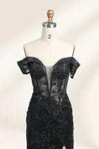 This photograph features a mannequin wearing an elegant, floor-length black lace gown. The gown has a sweetheart neckline, off-the-shoulder sleeves, and a high slit on one side, revealing a black thigh-high stocking. The intricate lace pattern is delicate and ornate, adding texture and visual interest. The mannequin stands against a plain, light beige background, emphasizing the dress's details. The number "2" is displayed on the mannequin's chest.03