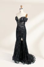 This photograph features a mannequin wearing an elegant, floor-length black lace gown. The gown has a sweetheart neckline, off-the-shoulder sleeves, and a high slit on one side, revealing a black thigh-high stocking. The intricate lace pattern is delicate and ornate, adding texture and visual interest. The mannequin stands against a plain, light beige background, emphasizing the dress's details. The number "2" is displayed on the mannequin's chest.05
