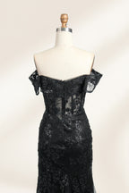 This photograph features a mannequin wearing an elegant, floor-length black lace gown. The gown has a sweetheart neckline, off-the-shoulder sleeves, and a high slit on one side, revealing a black thigh-high stocking. The intricate lace pattern is delicate and ornate, adding texture and visual interest. The mannequin stands against a plain, light beige background, emphasizing the dress's details. The number "2" is displayed on the mannequin's chest.06