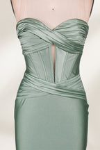 This photograph showcases a floor-length, strapless gown in a soft, mint green hue. The dress features a fitted bodice with a sweetheart neckline and a delicate, crisscrossed fabric pattern, accentuating the bust. The skirt flares out elegantly, ending in a subtle train. The gown is displayed on a mannequin with a wooden head and neck, set against a plain, light beige background. The fabric appears to be satin or silk, giving it a smooth, lustrous texture. 3
