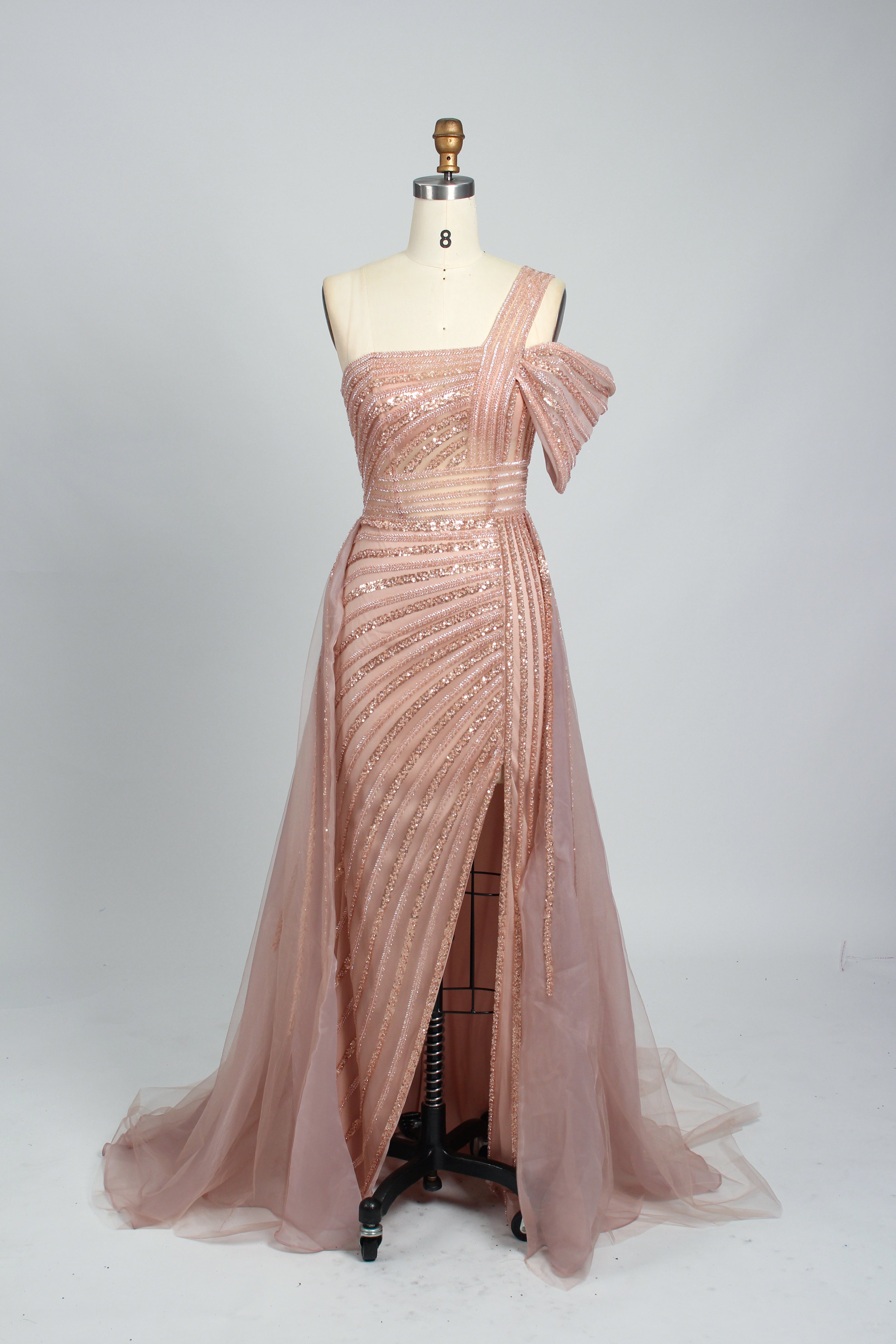Against a light - hued backdrop, a woman dons a teal sequin gown with an one - shoulder design. It features a bow - detailed strap, a sheer waist panel, and a high side slit. The sparkling sequins and unique silhouette radiate glamour, perfect for formal dinners or galas.7