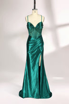 A mannequin displays a green satin gown against a light backdrop. It has thin straps, a sweetheart neckline, and a sheer bodice with beading. The mermaid skirt, featuring a high side slit, combines elegance and allure, perfect for formal galas.1