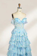 Photograph of a mannequin displaying a strapless, multi-layered, light blue tulle gown adorned with intricate floral embroidery. The gown has an off-shoulder neckline and a fitted bodice, cascading into voluminous, ruffled tiers. The background is plain white, highlighting the dress's delicate details. The mannequin is marked with the number "4" on its torso.4