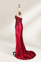 This photograph features a mannequin dressed in a strapless, floor-length, deep red satin evening gown. The gown is adorned with intricate sequin embroidery on the bodice and a high slit on the left side, revealing black stockings. The fabric has a smooth, luxurious texture. The mannequin stands on a black stool against a plain white background, creating a stark contrast that highlights the gown's vibrant color and detailed design. The overall style is elegant and glamorous, suitable for formal occasions.5