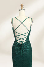 Photograph of a mannequin wearing a floor-length, deep green sequin dress with a plunging V-neckline, spaghetti straps, and a daring thigh-high slit on the left side. The dress has a fitted bodice and a flowing, slightly flared skirt. The mannequin is displayed against a plain white background with soft, diffused lighting creating gentle shadows.06