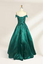 This is a photograph of a stunning, off-the-shoulder, floor-length evening gown displayed on a dress form. The gown is a rich, emerald green satin with intricate black floral lace embroidery on the bodice and hem. The dress features a sweetheart neckline, accentuating the bust, and a fitted waist that flares into a full, flowing skirt. The dress form is beige, with a wooden head and neck, and a metal neck ring. The background is a plain, light cream color, ensuring the dress remains the focal point.02