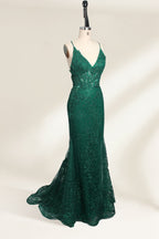 Photograph of a dark green, floor-length evening gown displayed on a white dress form. The gown features a deep V-neckline with thin spaghetti straps, a fitted bodice adorned with intricate lace detailing, and a flowing, slightly flared skirt. The dress showcases a rich, textured fabric with a shimmering effect, accentuating the luxurious and elegant style. The background is a plain, off-white color, ensuring the dress remains the focal point.04