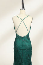 Photograph of a dark green, floor-length evening gown displayed on a white dress form. The gown features a deep V-neckline with thin spaghetti straps, a fitted bodice adorned with intricate lace detailing, and a flowing, slightly flared skirt. The dress showcases a rich, textured fabric with a shimmering effect, accentuating the luxurious and elegant style. The background is a plain, off-white color, ensuring the dress remains the focal point.05